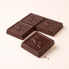 Four dark chocolate squares with embossed unicorn designs, arranged on a clean off-white background.