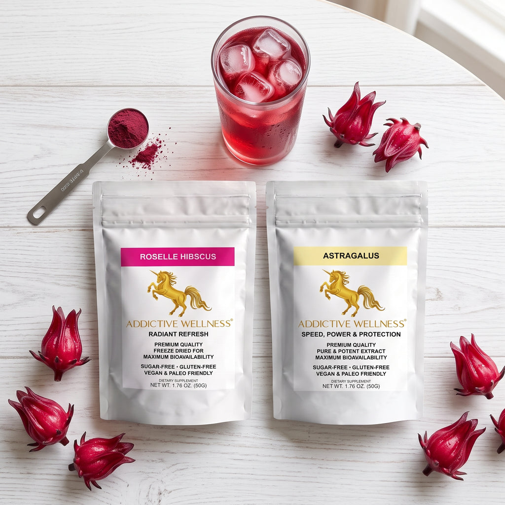 Two stand-up pouches of Addictive Wellness herbal supplements on a white wooden surface, surrounded by red dragon fruit and a glass of red drink with ice. The left pouch is labeled Robelle Hibiscus with a pink label, and the right pouch is labeled Astragalus with a yellow label.
