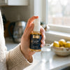 Hand holding a bottle of Liposomal Glutathione Lemon Mint in a sunny kitchen