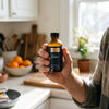 Hand holding a small bottle of Quicksilver Liposomal Vitamin C in a bright kitchen