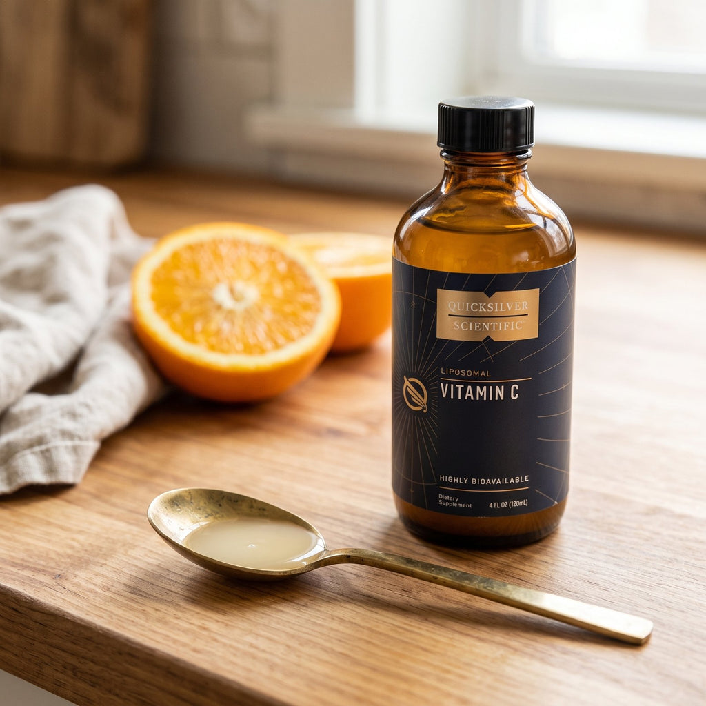 One teaspoon of Liposomal Vitamin C in a brass spoon with the bottle and a halved orange on a kitchen counter