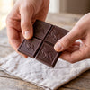 Hands snapping a square off an Addictive Wellness unicorn chocolate bar